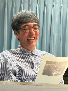 おぎやはぎの小木博明が眼鏡をかけ、ラジオの原稿を見ながら笑っている写真